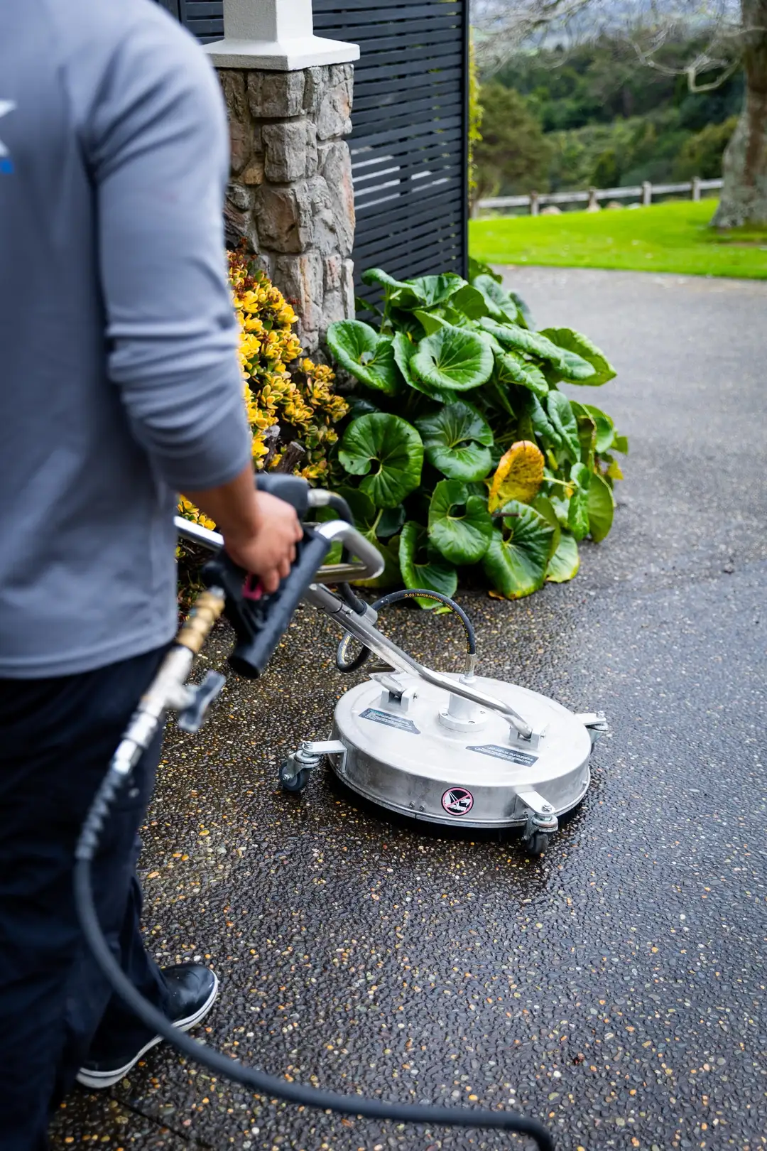 Close up: the surface cleaner on wet concrete, the hose and wand in Logan's hands