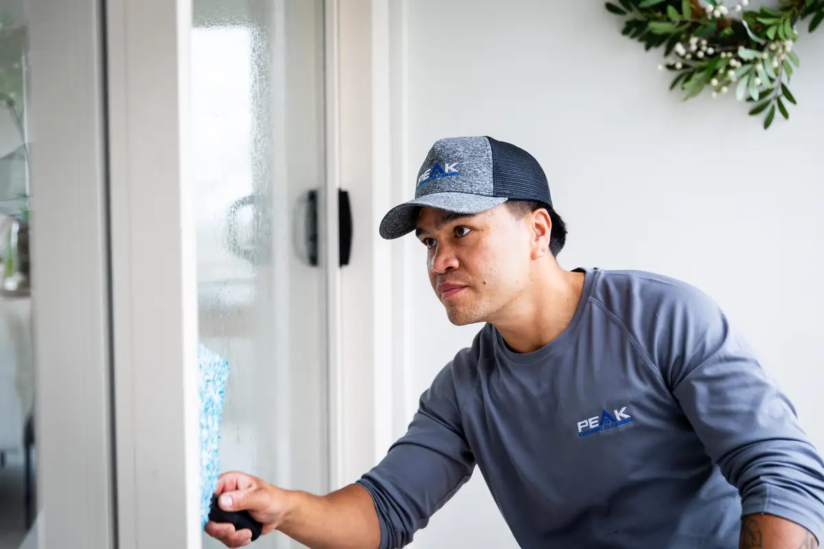 Logan Howard in his PEAK cap and shirt, cleaning the glass of a door